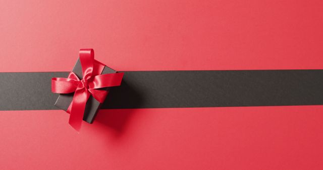 Black gift box wrapped with a vibrant red ribbon on a contrasting red and black background. Ideal for holiday promotions, gift-related advertisements, and celebratory event themes. Highlight elegant and minimalist packaging design for marketing materials or social media content.
