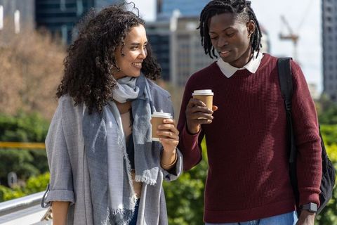 Young professionals walking and chatting while holding takeaway coffee cups in city park