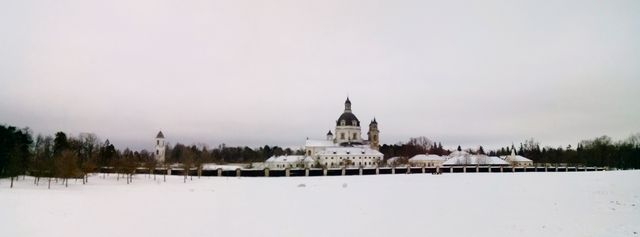 Panoramic view of a historic church and surrounding buildings covered in snow during winter. Ideal for use in travel guides, postcards, or religious event promotions. Perfect for conveying a serene and peaceful winter scene.