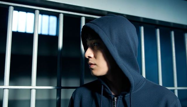 Young man in hooded sweatshirt standing by prison bars at dimly lit window