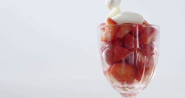 Close-up of fresh strawberries with cream in glass against white background
