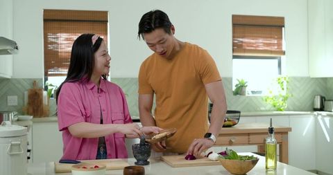 Couple cooking together on bright kitchen island preparing fresh meal chopping vegetables