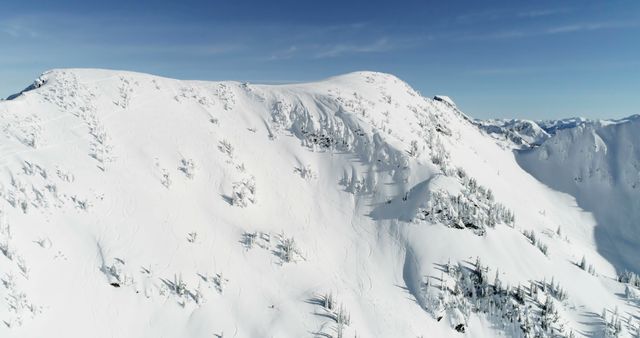 Aerial view of a snow-covered mountain under a clear blue sky. The pristine white landscape suggests a tranquil yet adventurous outdoor setting.