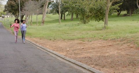 Two women jogging side-by-side on park road carrying water bottles and wearing leggings