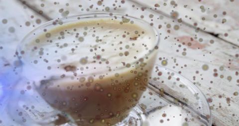 Macro frothy latte in glass cup on vintage whitewashed table with artistic speckle bokeh