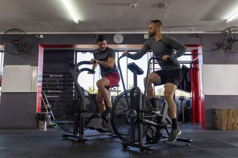 Intense duo pushing fan bikes during interval training in modern gym for endurance workout