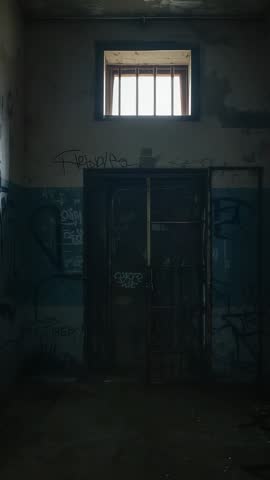 Vertical video showing abandoned cell with high barred window and rusted security door