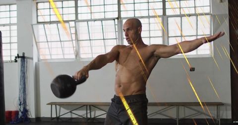 Shirtless man swinging kettlebell in gym performing single-arm swing for strength training