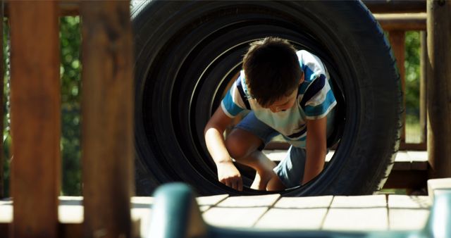 Young boy exploring and playing in oversized tire on playground. Useful for illustrating outdoor activities, childhood fun, adventure, and playground safety. Can be used in websites, blogs, or print materials focusing on kids' activities, outdoor play, and healthy childhood development.