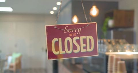 Retro closed sign hanging on cafe door with warm pendant lights and cozy interior