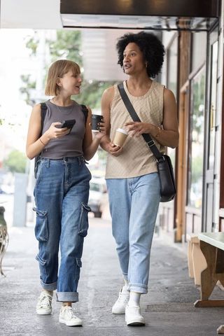 Young diverse friends walking and chatting with coffee and smartphone on city sidewalk