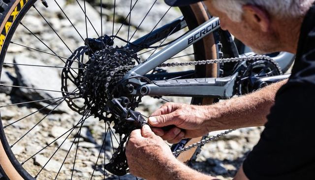 Older cyclist repairing mountain bike derailleur and cassette on rocky trail close-up