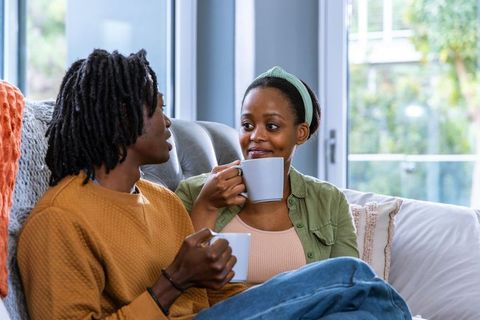 African american couple sharing coffee on couch, cozy intimate conversation at home