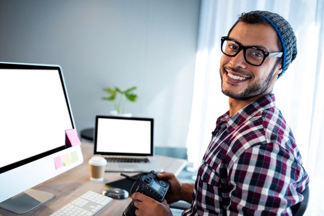 Attractive hipster smiling at camera while working at desk in studio