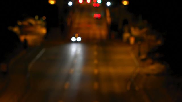 High-angle view capturing cars moving on a city road at night with vibrant bokeh effects from distant lights. Perfect for usage in projects related to urban night life, traffic flow studies, or atmospheric backgrounds conveying motion in a city night setting.