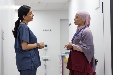 Two nurses discussing patient care in hospital corridor near x-ray sign