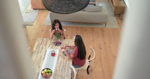 Diverse women sharing tea at contemporary wooden dining table, cozy top-down interior