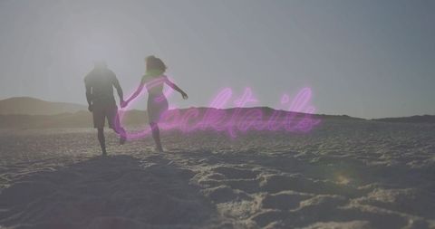 Backlit couple running on beach holding hands with neon cocktails sign at sunrise