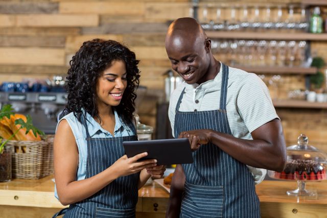 Smiling cafe staff using a digital tablet at the counter. Ideal for illustrating teamwork, modern technology in small businesses, customer service, and hospitality industry. Useful for articles, advertisements, and promotional materials related to cafes, restaurants, and teamwork.