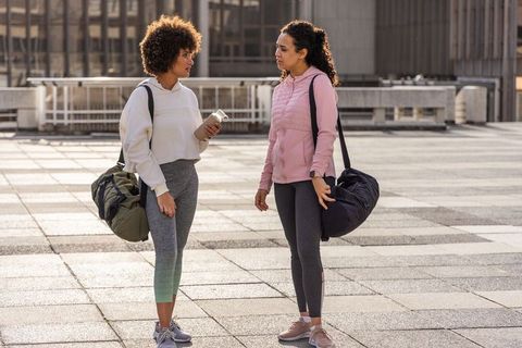 Friends chatting after workout on rooftop terrace carrying duffel bags and water bottle