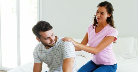 Woman Offering Comfort to Man on Bed in Light-Filled Bedroom