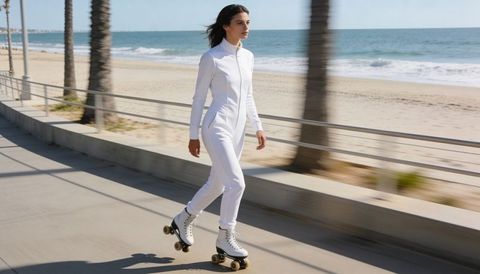 Woman roller skating on sunny seaside promenade wearing white jumpsuit and vintage skates
