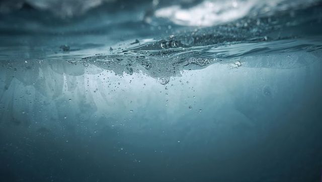 Underside sea ice beneath waterline with rising bubbles and ethereal polar light