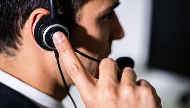 Hispanic customer service agent pressing headset earcup while speaking on call at desk