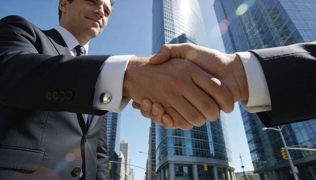 Businessmen shaking hands in downtown skyscraper district with cufflinks and lens flare