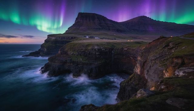 Aurora over rugged sea cliffs and waterfall on coastal plateau under violet night sky