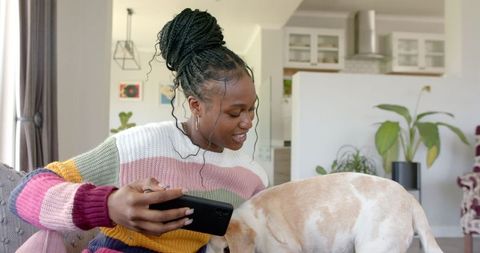 Young woman with braided hair using smartphone with pet dog at home