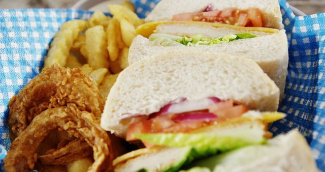 A delicious-looking sandwich with fresh vegetables and crispy chicken is served alongside golden French fries and onion rings, with copy space. Perfect for a casual lunch, this meal combines comfort food with a touch of freshness.