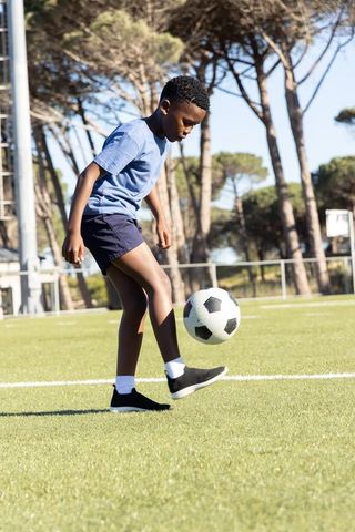 African american boy dribbling soccer ball on grass field during sunny outdoor training