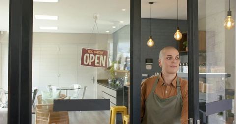 Bald barista opening glass door with open sign welcoming customers into cozy modern cafe