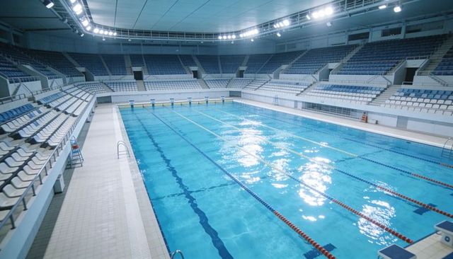Shimmering olympic-size indoor swimming pool with empty stands and competition lanes
