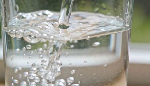 Pouring clear water filling glass with bubbles and ripples close-up natural light