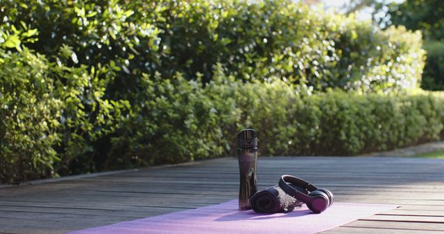 Water bottle, headphones, towel and yoga mat on deck in sunny garden, copy space, slow motion. Yoga, wellbeing, fitness and healthy lifestyle.
