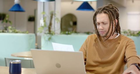 African American man reading document and reacting with concern while working at laptop