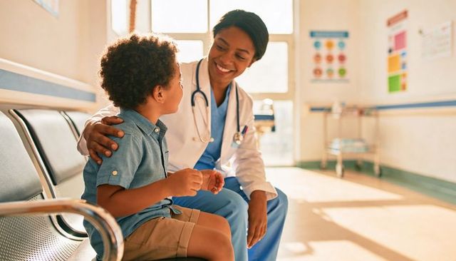 Smiling pediatrician comforting young patient in clinic waiting area with stethoscope