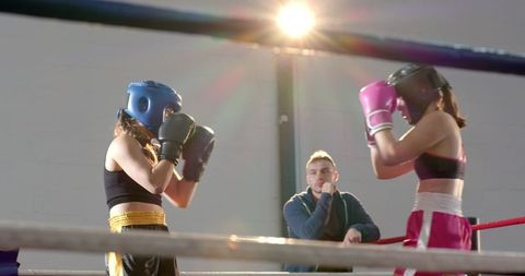 Female boxers sparring in ring with coach observing intense training session