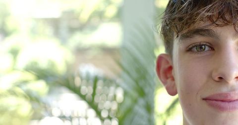 Smiling teen male headshot at sunlit window with palm leaf bokeh and ample copy space