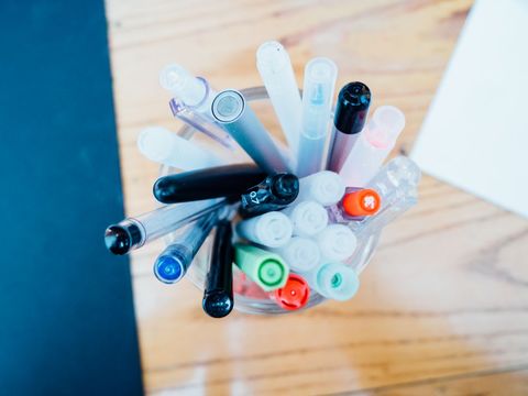 Colorful Assortment of Pens in Glass Holder on Wooden Desk
