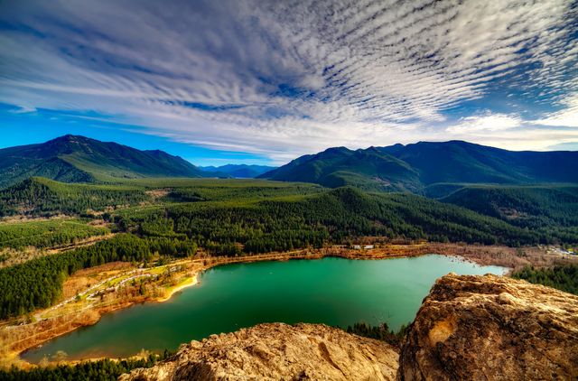 This stunning scenic panorama captures a turquoise lake nestled among lush green mountains with a dramatic sky above. Ideal for travel brochures, nature blogs, outdoors adventure promotions, and landscape photography collections. Perfect for emphasizing tranquility, natural beauty, and outdoor recreation.