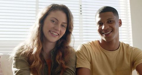 Sunlit young couple sitting together on sofa smiling and sharing relaxed moment