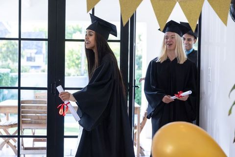 Joyful Students in Caps and Gowns Holding Diplomas Indoors
