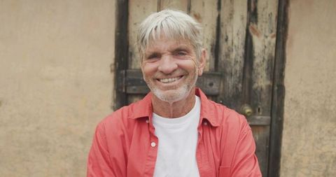 Smiling senior man wearing red shirt in front of weathered door and textured wall