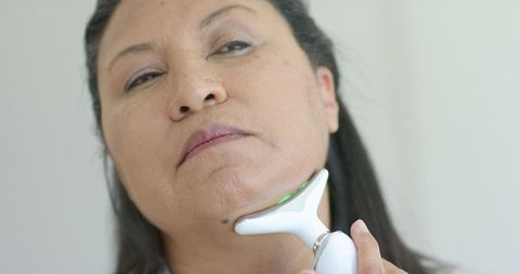African american woman using handheld y-shaped led facial device on chin for skin tightening