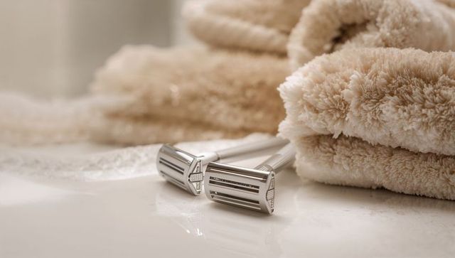 Twin chrome double-edge razors resting on glossy vanity with plush beige towels