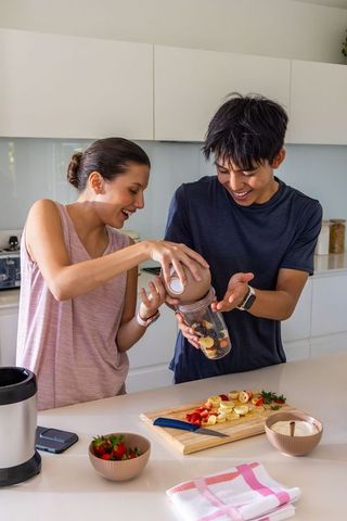 Diverse couple preparing fruit smoothies at modern kitchen island with portable blender