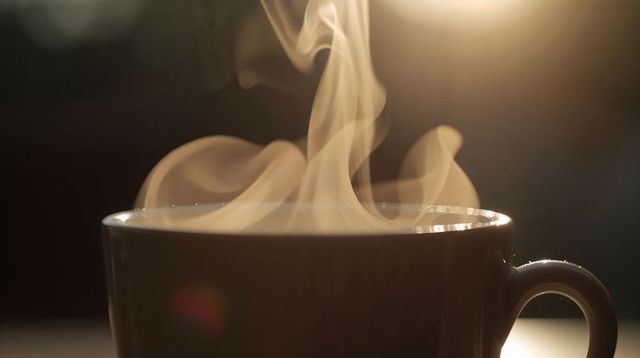 Steam rising from white ceramic mug with warm backlight and rim reflections